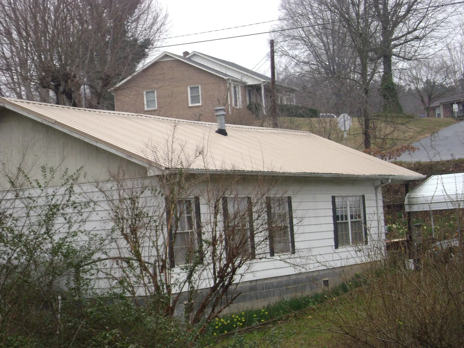 Tan metal roof on a white sided house set into a hillside — Commercial Roofing by Roofing Brothers in Girard